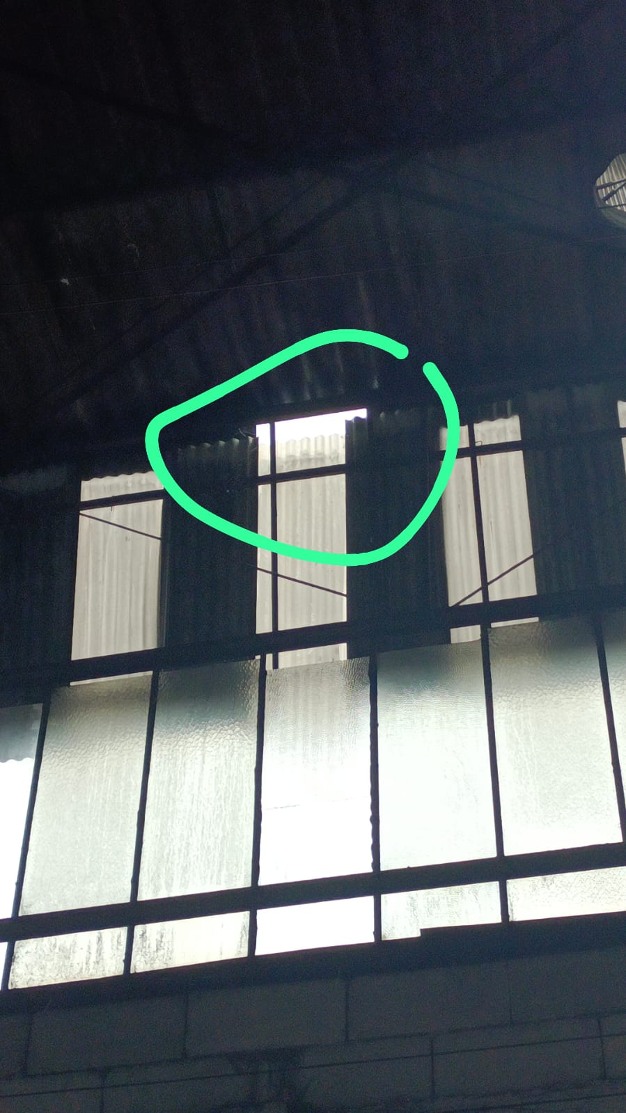 Interior de galpão com janela basculante próxima ao telhado, com círculo verde destacando a área da calha